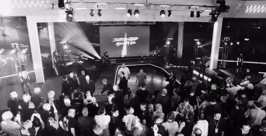 A black and white photo of a crowd at November 2025 Tesla Shareholder Event with Elon Must on Stage answering audience questions